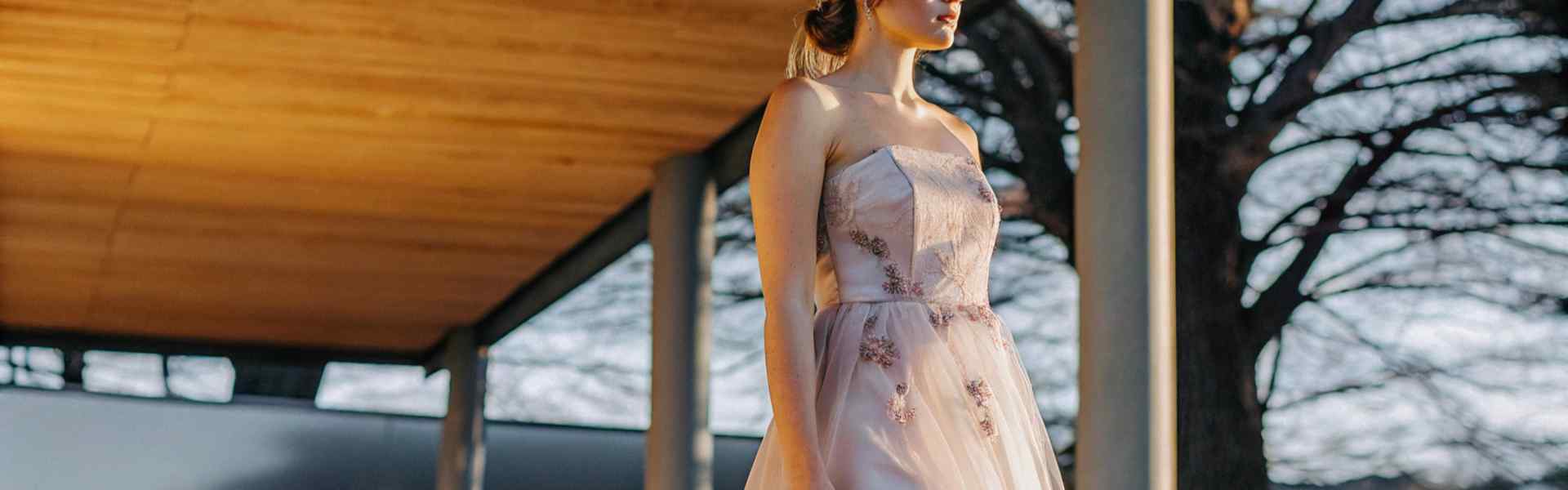 Woman in a blush pink strapless dress with floral details standing outdoors.