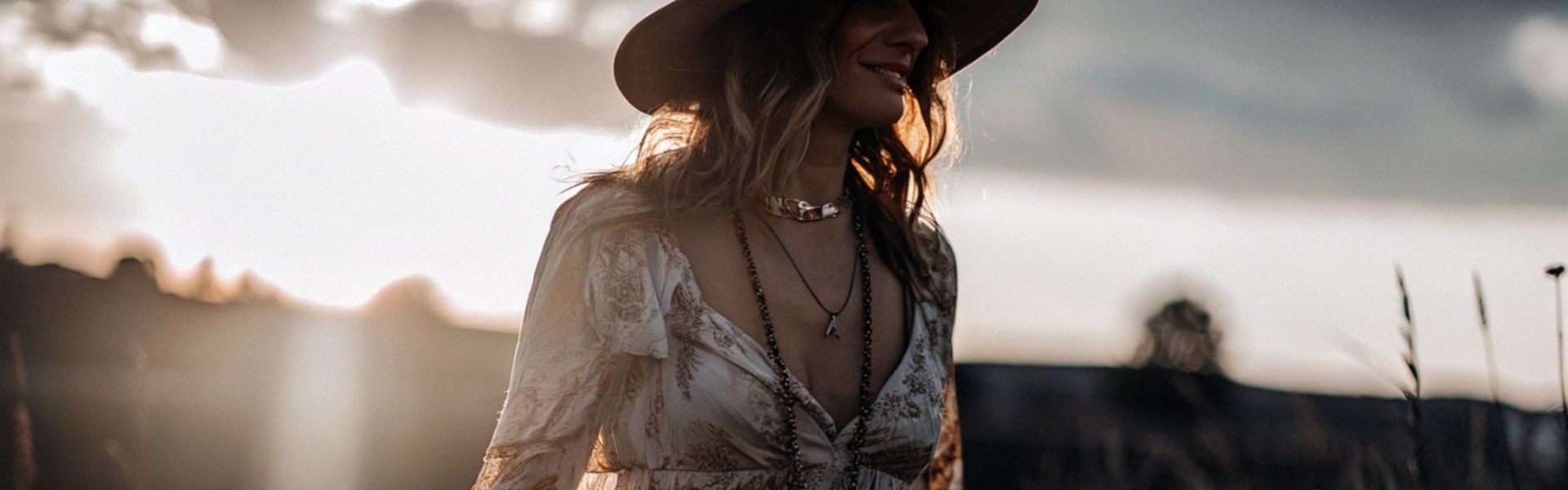 Woman in a flowing bohemian dress and wide-brimmed hat enjoying the sunset in a field.