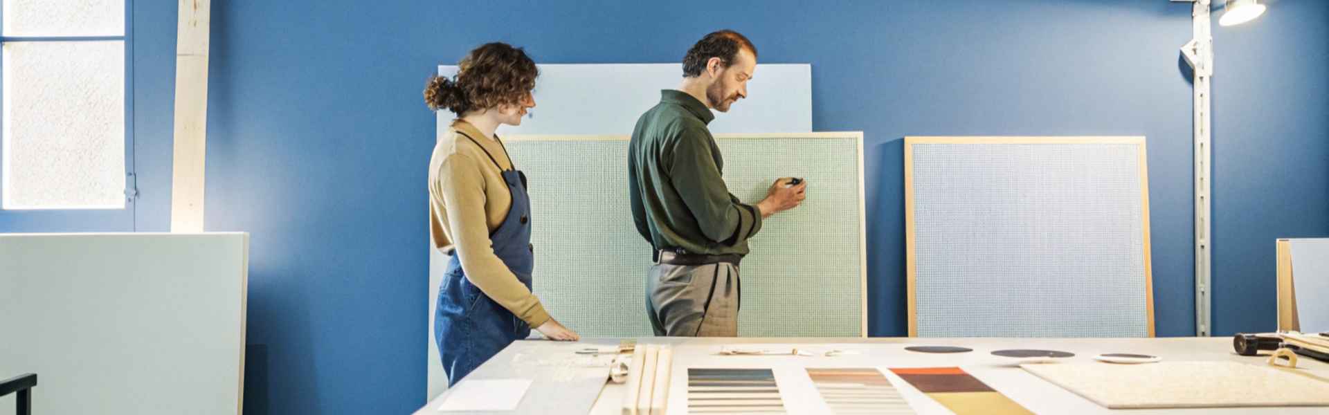 Two individuals working together on a textured panel in a blue-walled design studio.