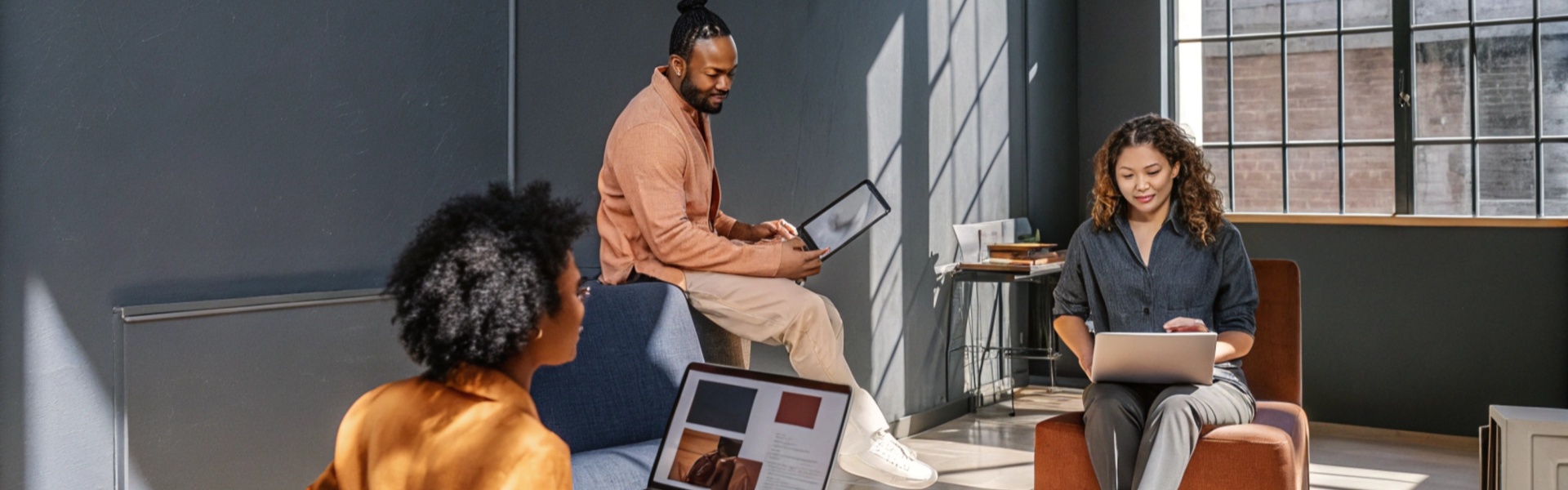 Three colleagues using laptops and tablets in a bright, modern office space.