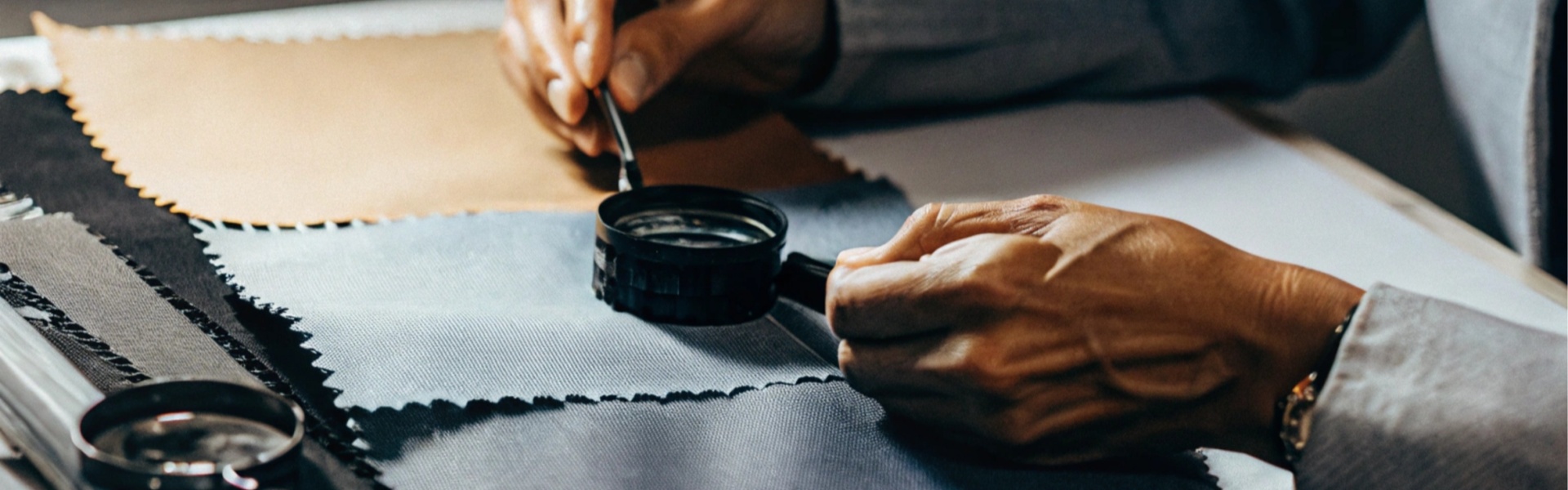 Person examining fabric swatches with a magnifying glass.