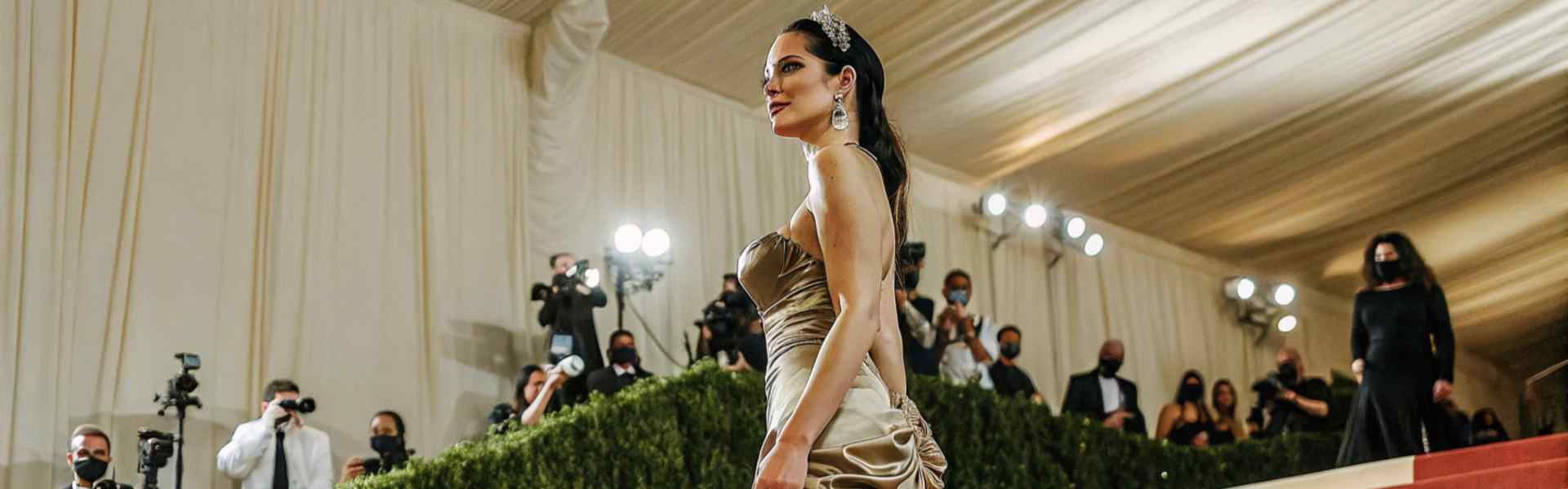 Woman in a gold strapless gown ascending the red carpet stairs under bright lights.