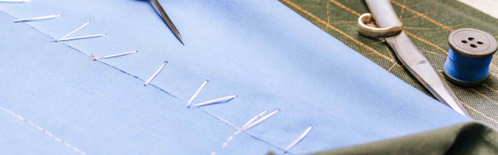 A close-up of a blue fabric being hand-stitched with tools like scissors and thread.