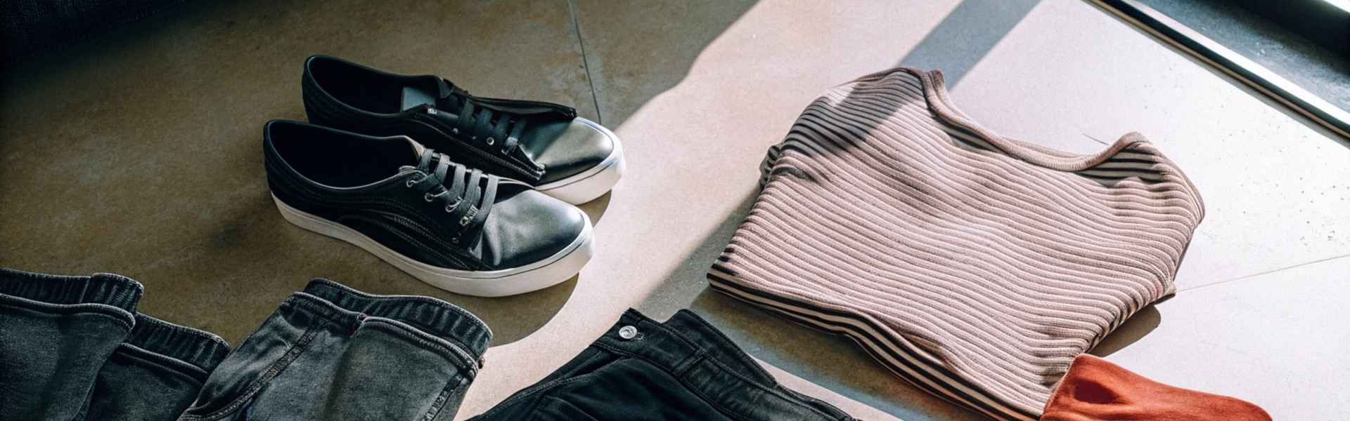 Folded casual clothing and black sneakers arranged on a sunlit surface.