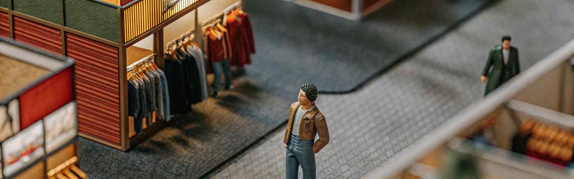 Miniature model of a shopping mall with tiny figures browsing clothing stores.