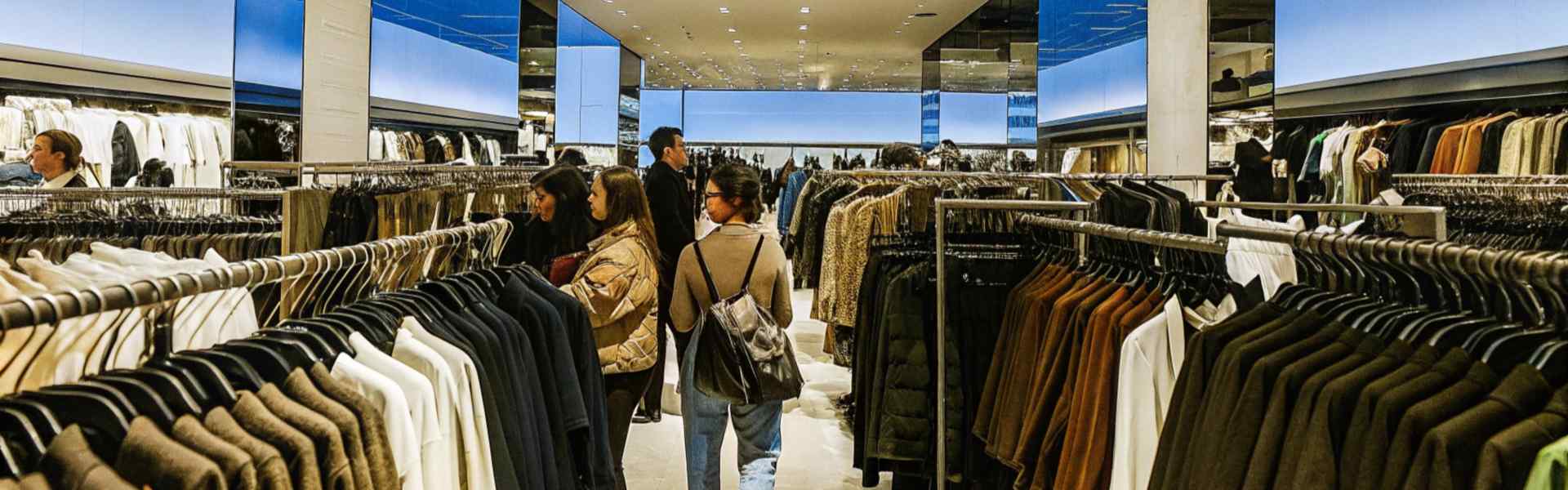 Shoppers browsing racks of clothes in a spacious and modern store with blue accents.