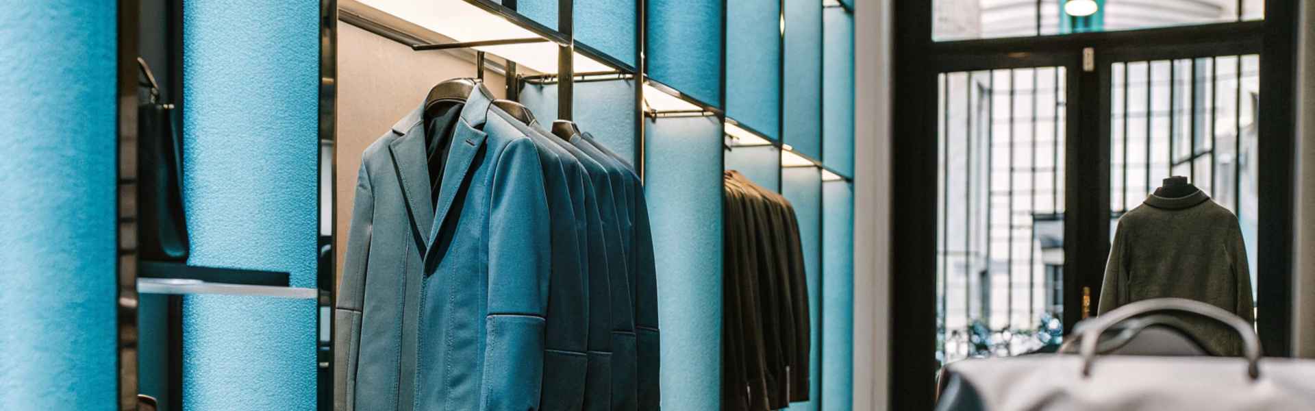 A retail wall showcasing tailored blue suits and minimalist leather bags.