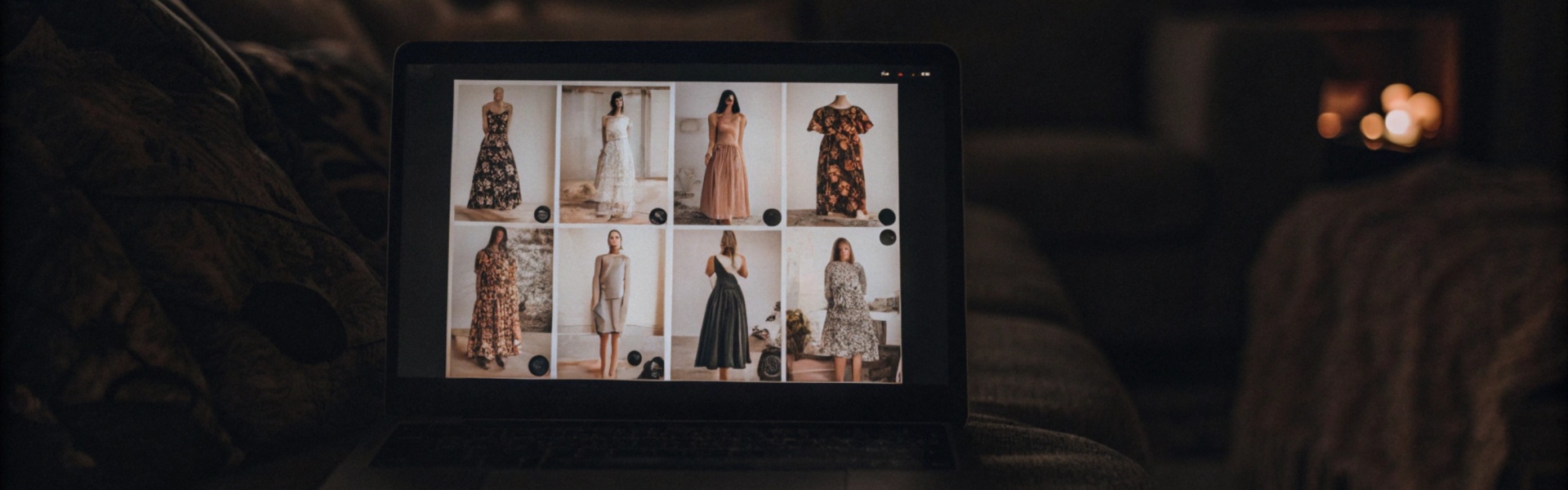 Laptop displaying a clothing catalog on a cozy couch with dim candlelit ambiance.