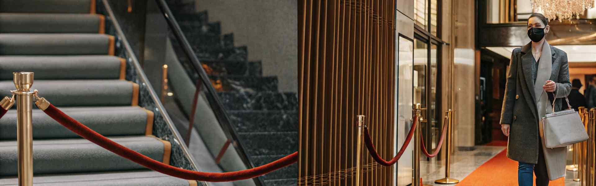 Red carpet with gold stanchions leading up marble stairs, a woman walking elegantly in a modern hallway.