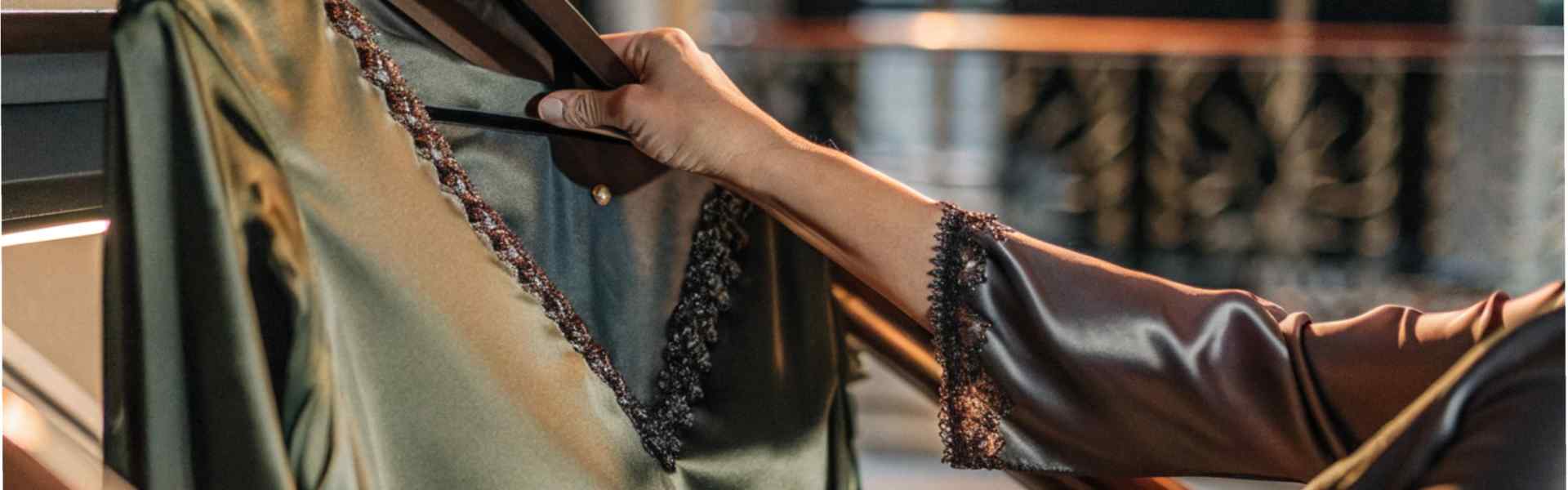 Close-up of a hand holding a green satin dress with lace trim on a hanger.