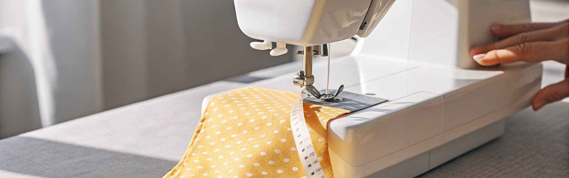 A sewing machine working on yellow polka-dotted fabric with scissors and a measuring tape nearby.