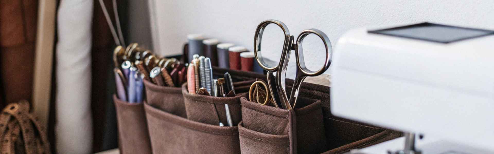 A leather organizer holding scissors, threads, and sewing tools next to a sewing machine.