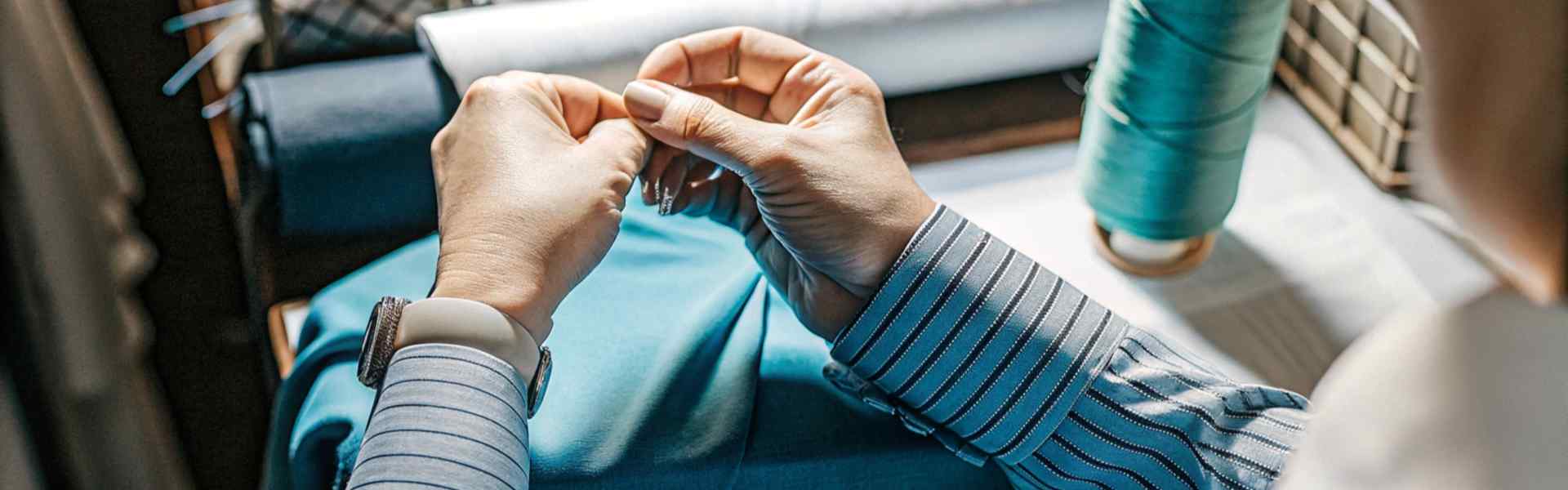 Person working on blue fabric with thread in a sewing studio.