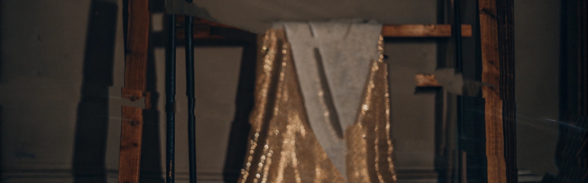 Glittering gold fabric draped on a wooden frame in a dimly lit room.