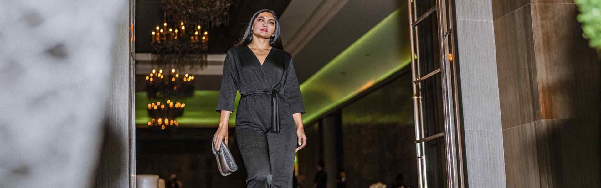 Woman in a black jumpsuit walking down a green carpet at an elegant venue.