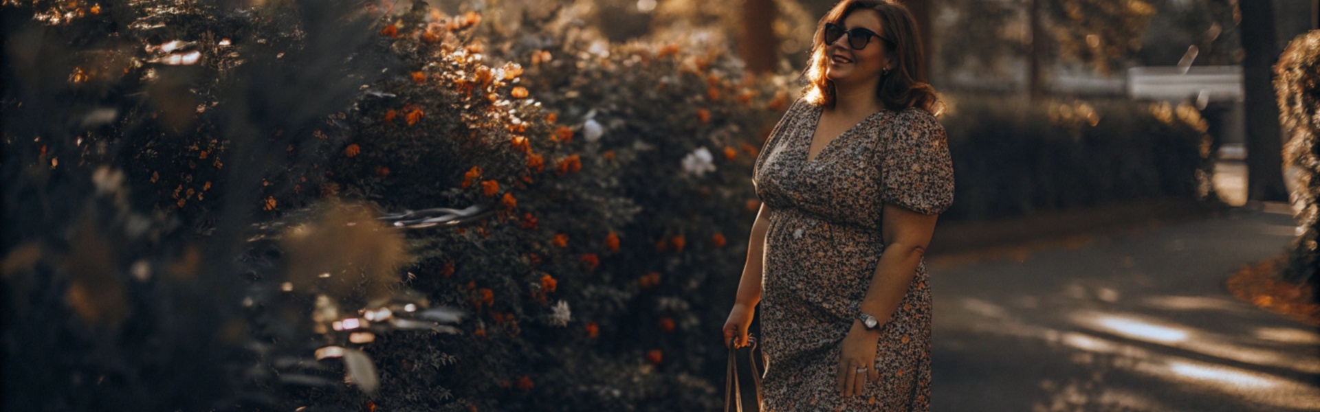 Woman in a floral dress and white sneakers enjoying a walk in a sunlit garden.