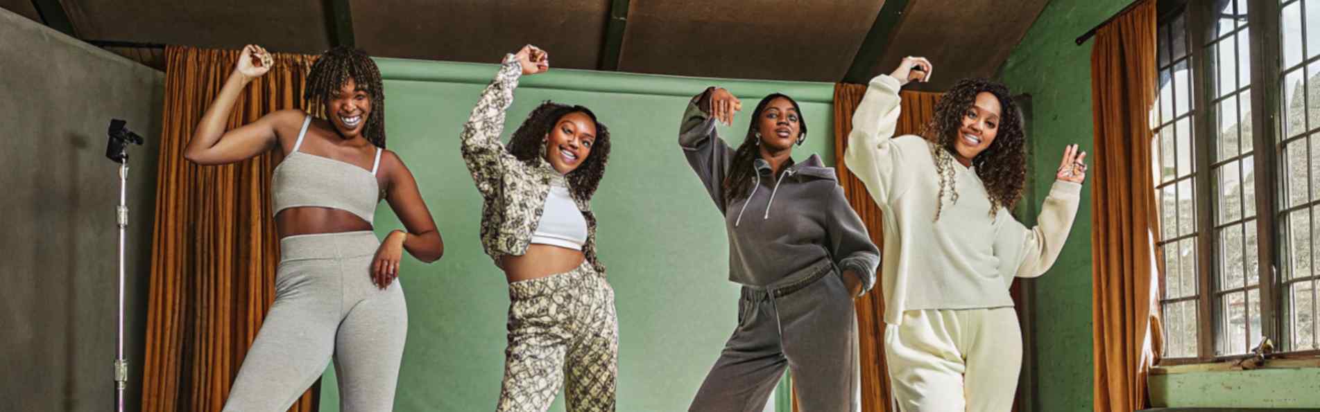 Four women in modern activewear posing confidently in a studio with a green backdrop.