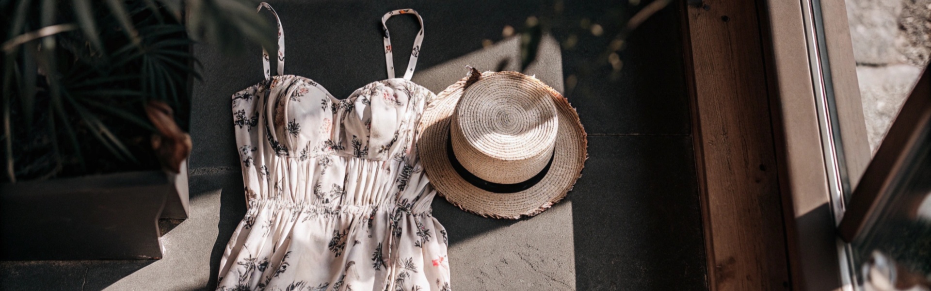 Floral summer dress with straw hat and white sneakers laid on the floor.