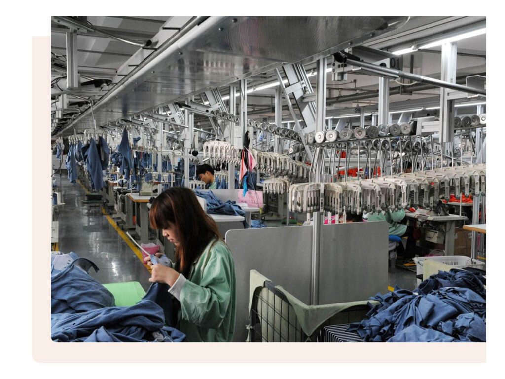 Workers in a garment factory handling fabrics and garments with automated overhead hanging systems.