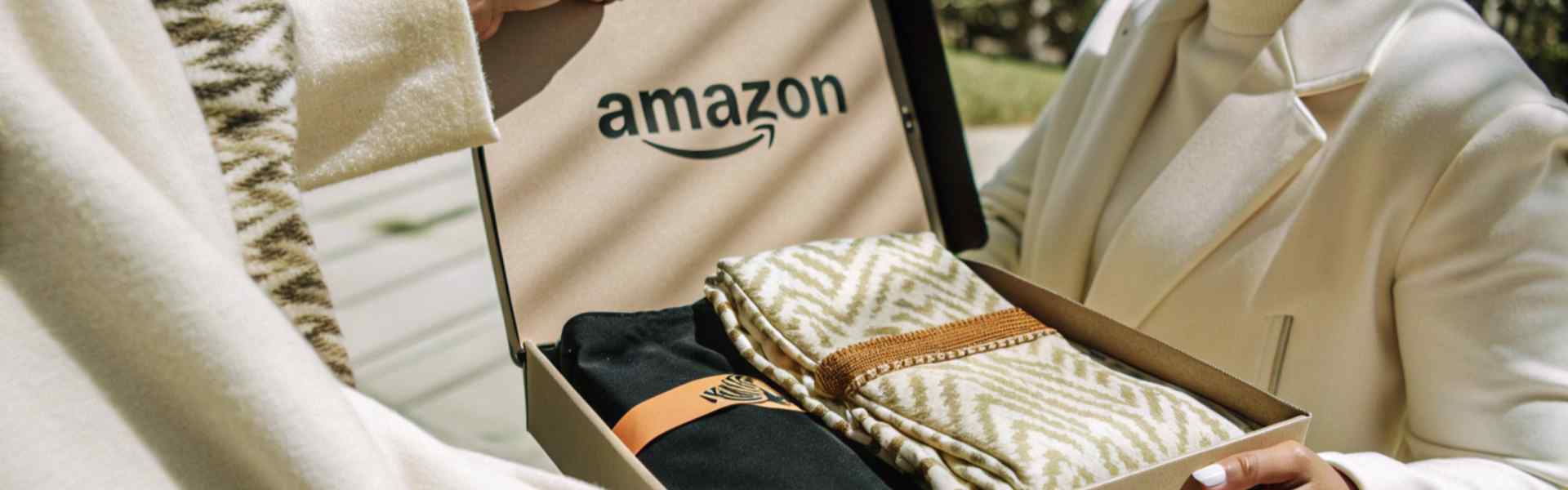 A person presenting an Amazon-branded gift box containing folded blankets with elegant patterns.