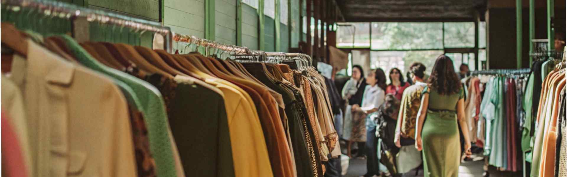 A green-lit indoor market showcasing colorful clothes on racks with shoppers in the background.