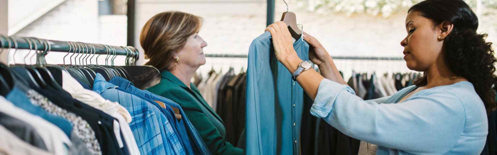 Two women looking at a blue shirt and other garments in a clothing store.