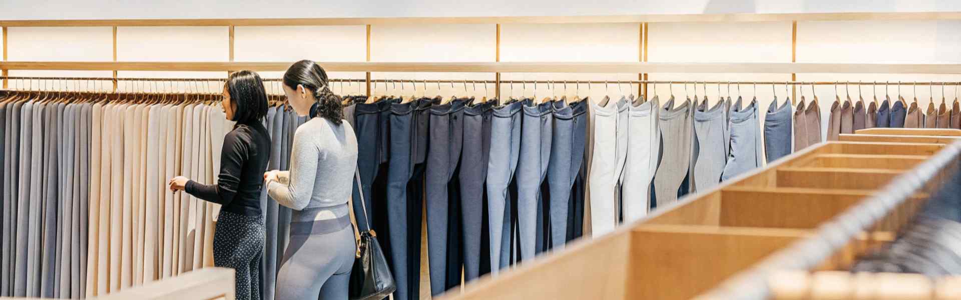 Two women examining racks of leggings and activewear in a bright store.