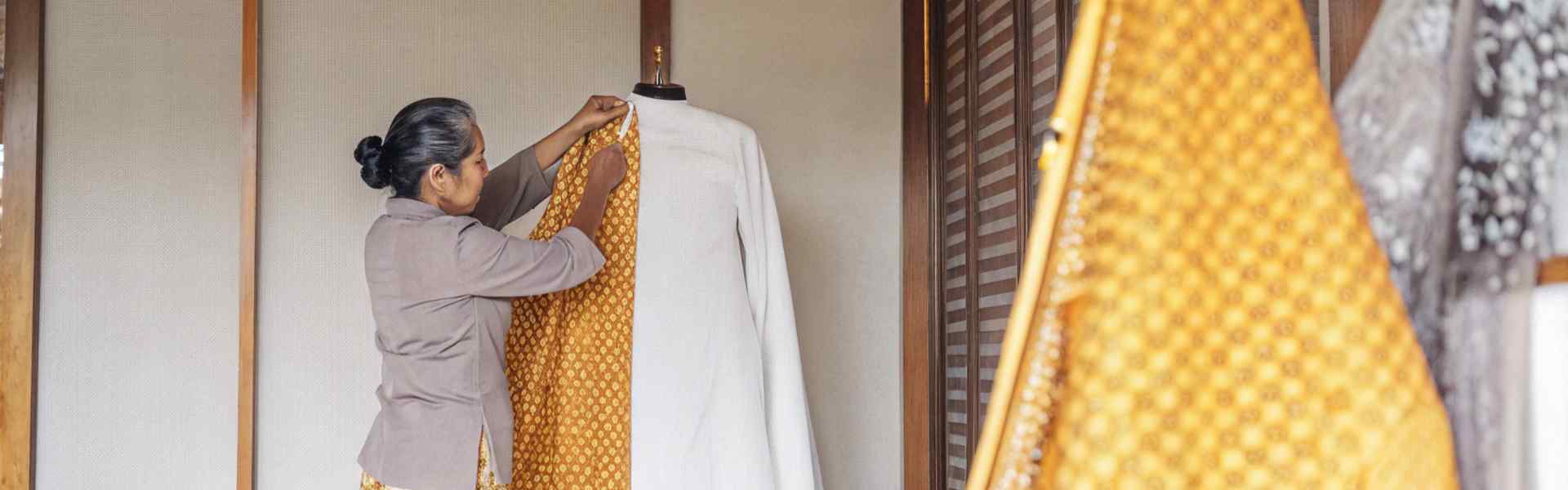 Woman draping orange patterned fabric on a white mannequin in a studio setting.