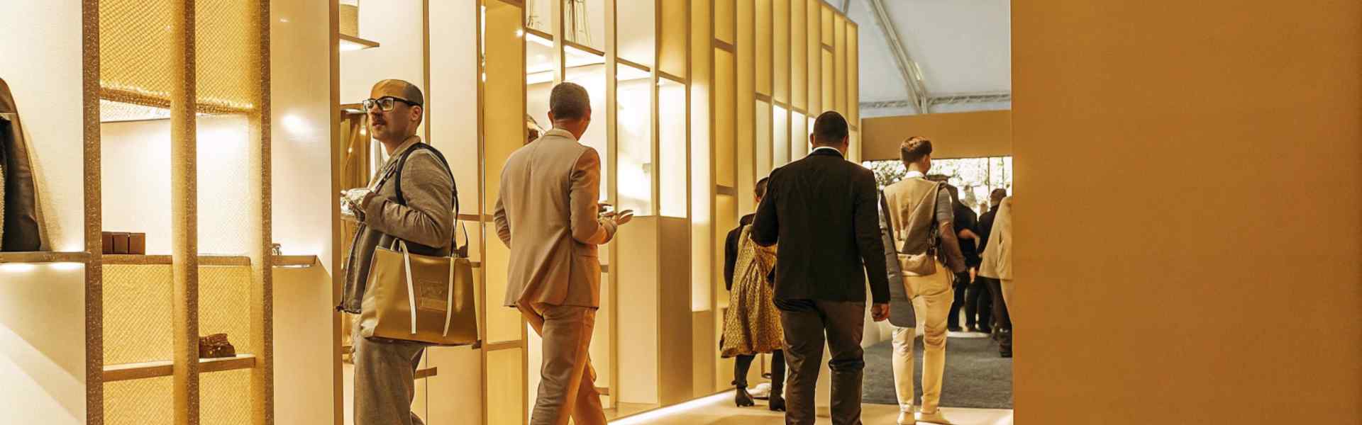 Visitors walking through a brightly lit exhibition hall with golden displays.