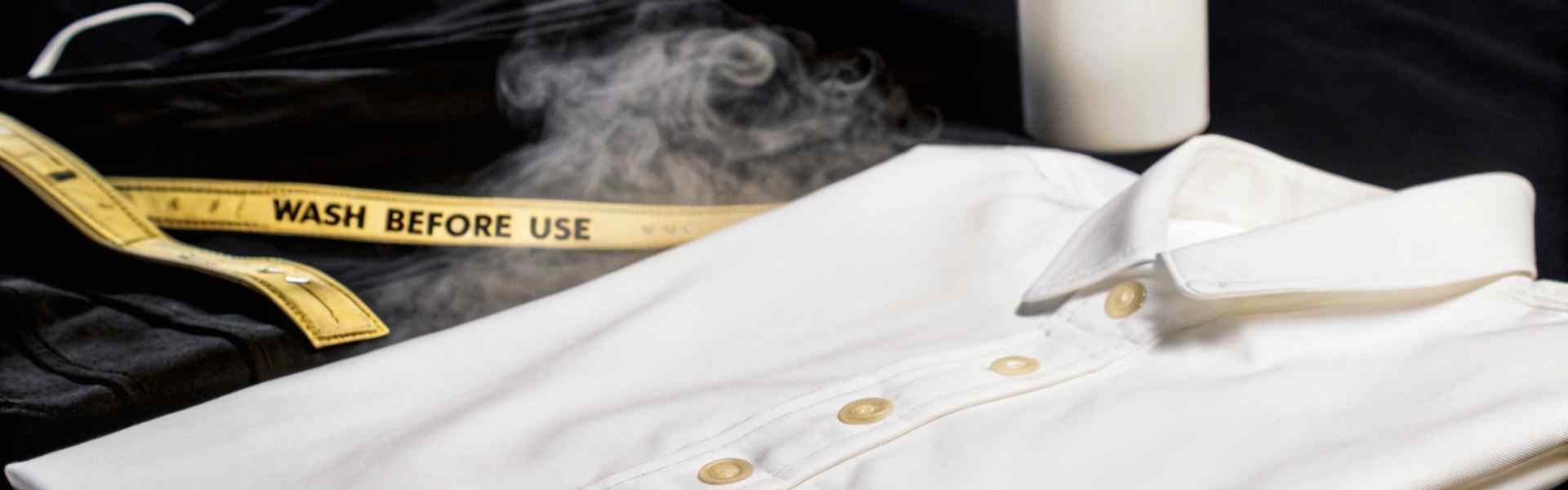 A white shirt with steam, a fabric care bottle, and a measuring tape with "Wash Before Use" written on it.