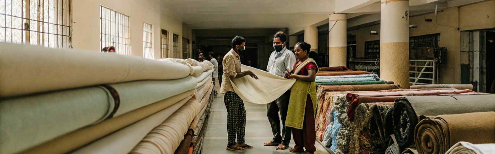 Workers and customers examining rolls of fabric in a spacious textile warehouse.