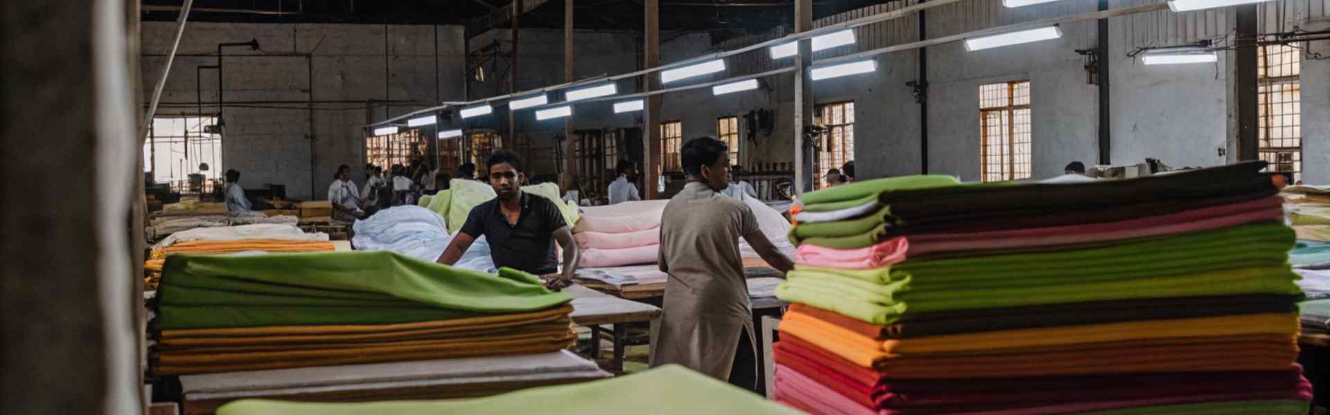 Workers sorting colorful fabric piles in a textile factory with industrial lighting.