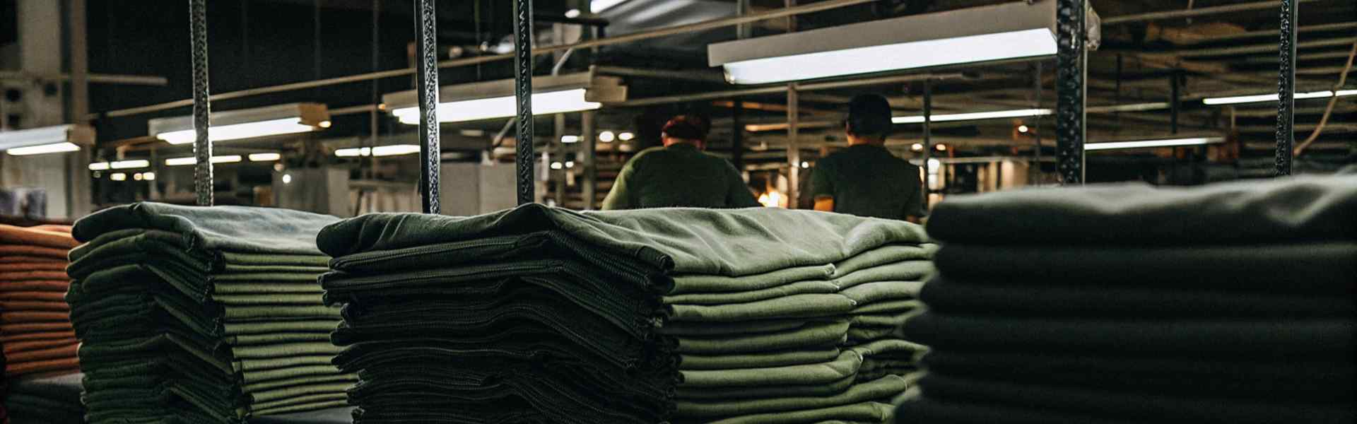 Stacks of green fabric neatly arranged in a dimly lit factory.