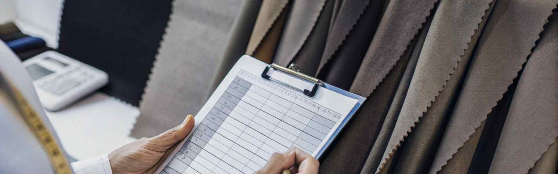 A person holding a clipboard while inspecting fabric samples in various shades.