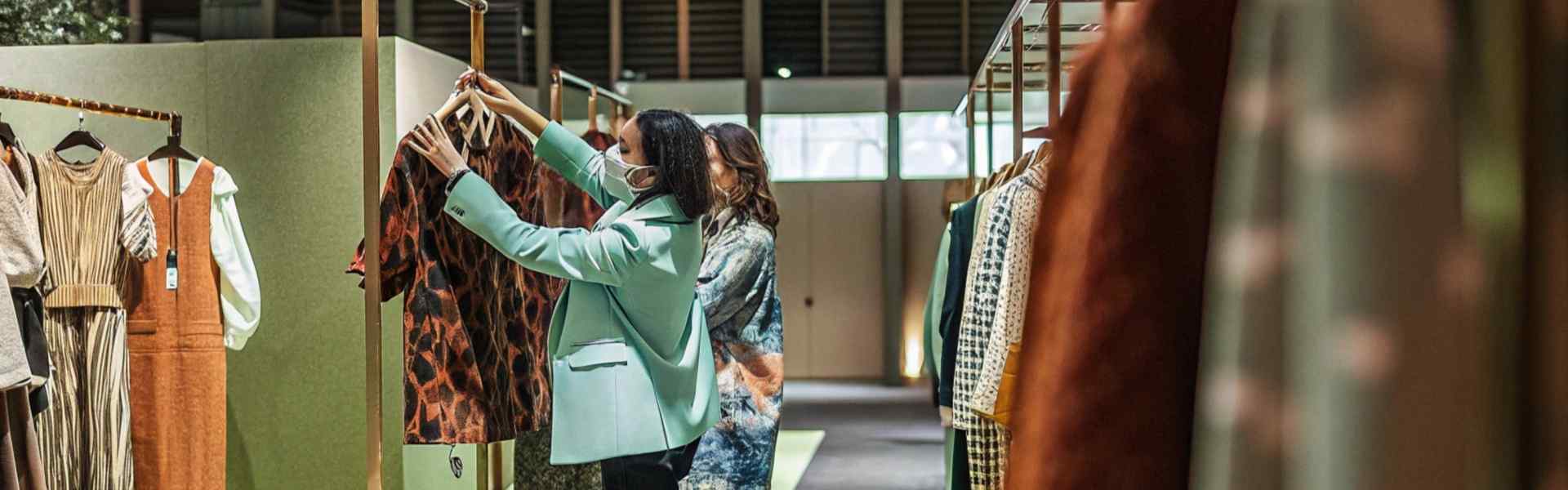 Two women browsing garments on a clothing rack in a well-lit showroom.