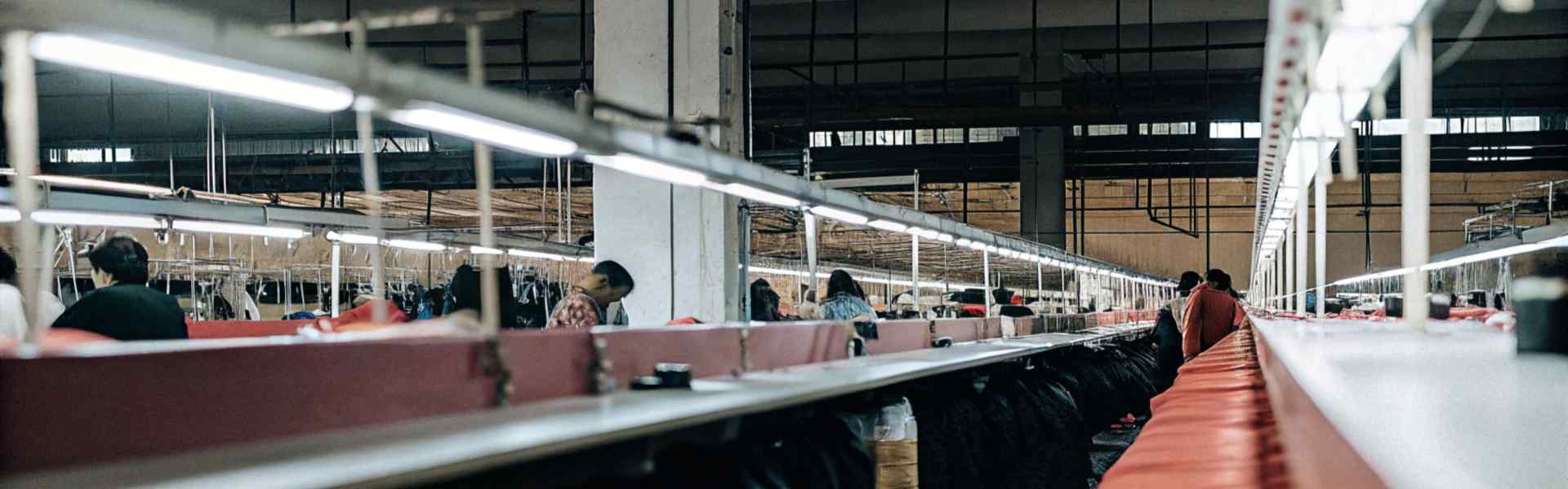 A long garment production line in a factory with workers processing clothes under bright lights.