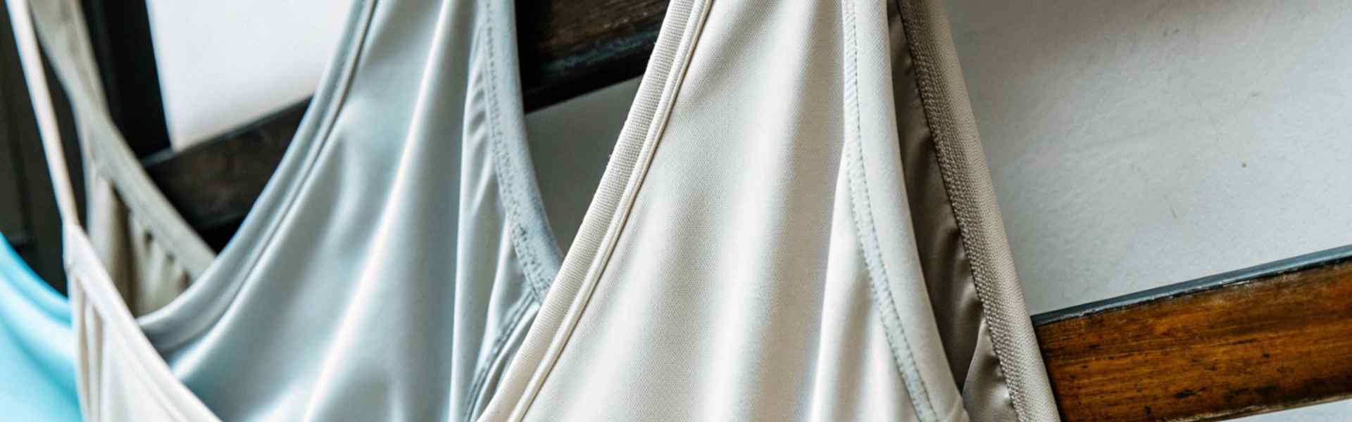 Close-up of light-colored camisoles hanging on a wooden rack.