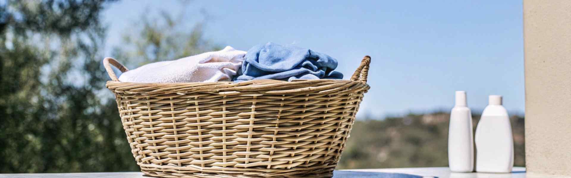 A wicker laundry basket filled with blue and white clothes placed on an outdoor ledge under a clear blue sky.