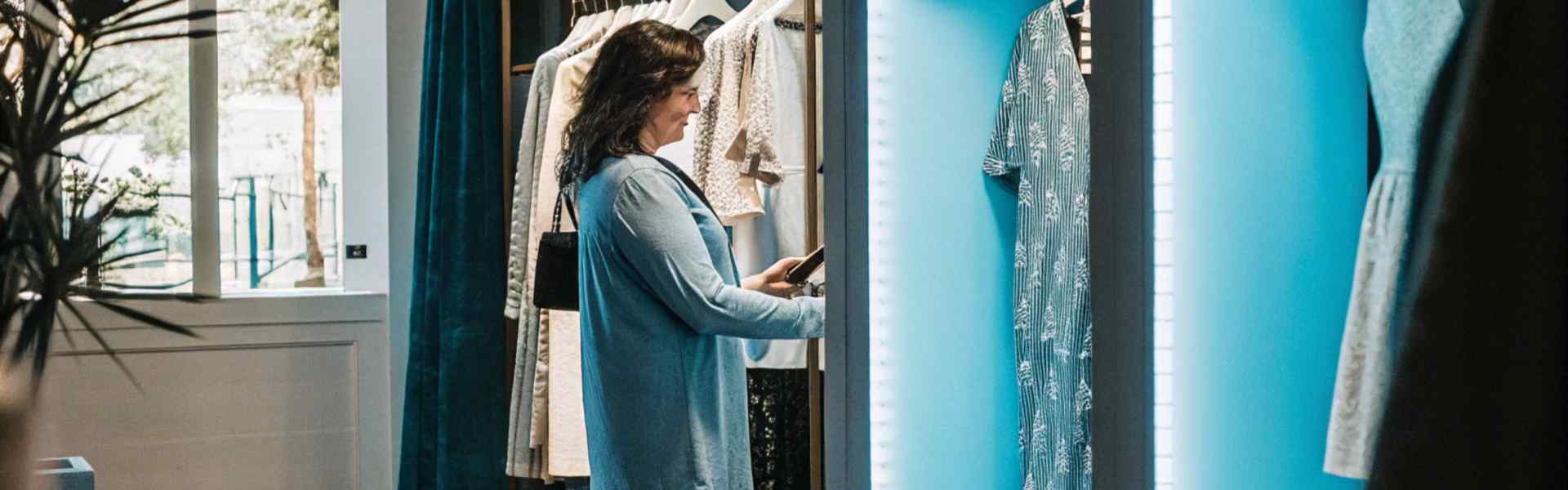 Woman browsing clothing racks in a stylish boutique with illuminated display sections.