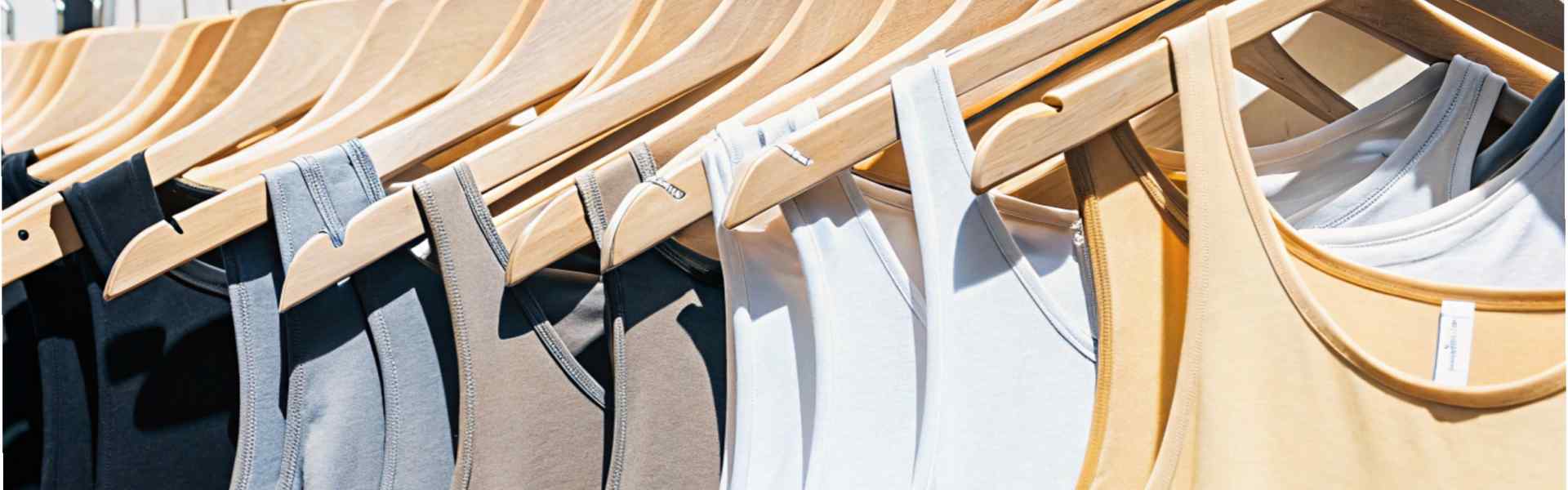 Row of tank tops in neutral colors on wooden hangers in sunlight.