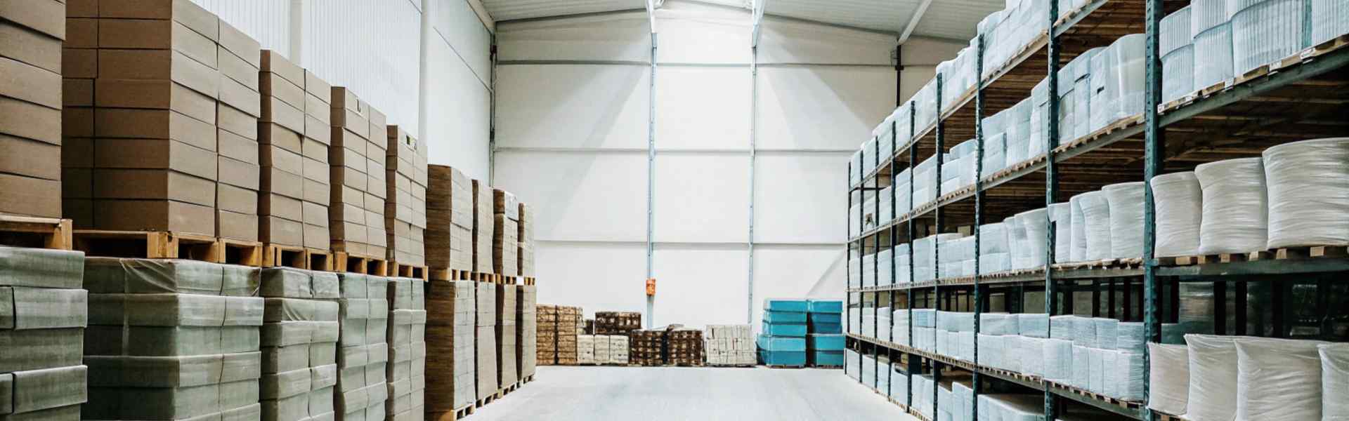 Bright warehouse with neatly stacked pallets of boxes and rolls of material.