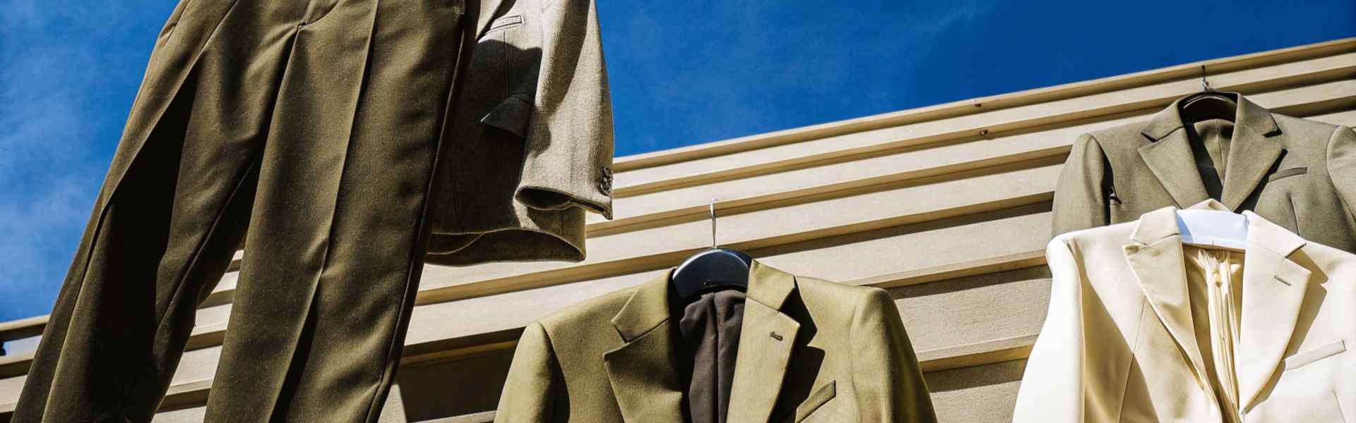 Suits and trousers hanging outdoors under a bright blue sky.