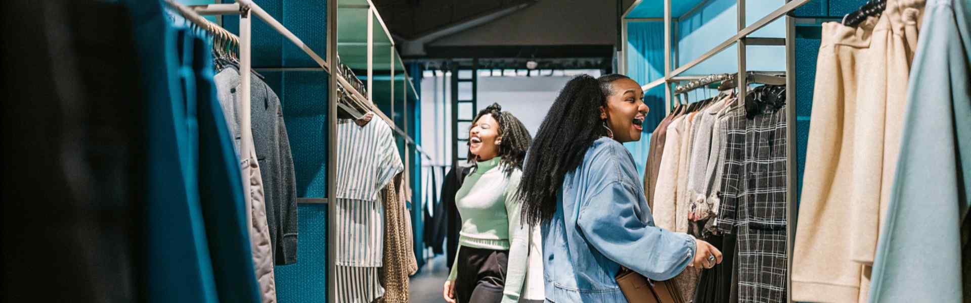 Two women enjoying shopping in a modern clothing store with blue shelves and hanging garments.