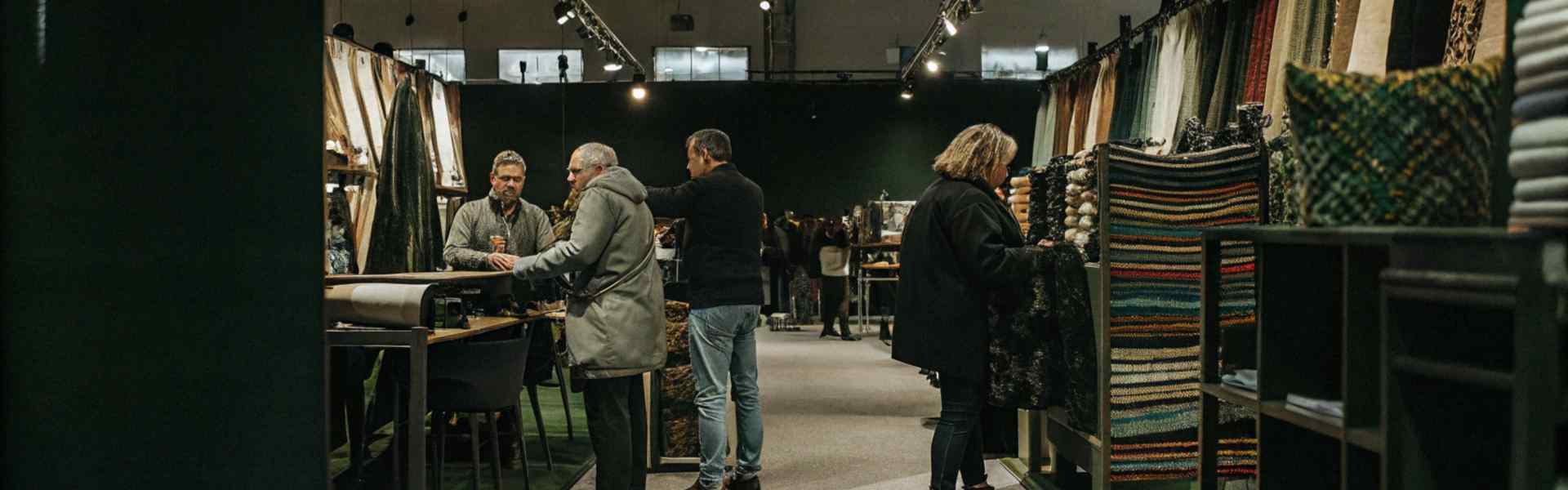 Visitors exploring fabrics and textiles at an indoor trade show with booths and displays.