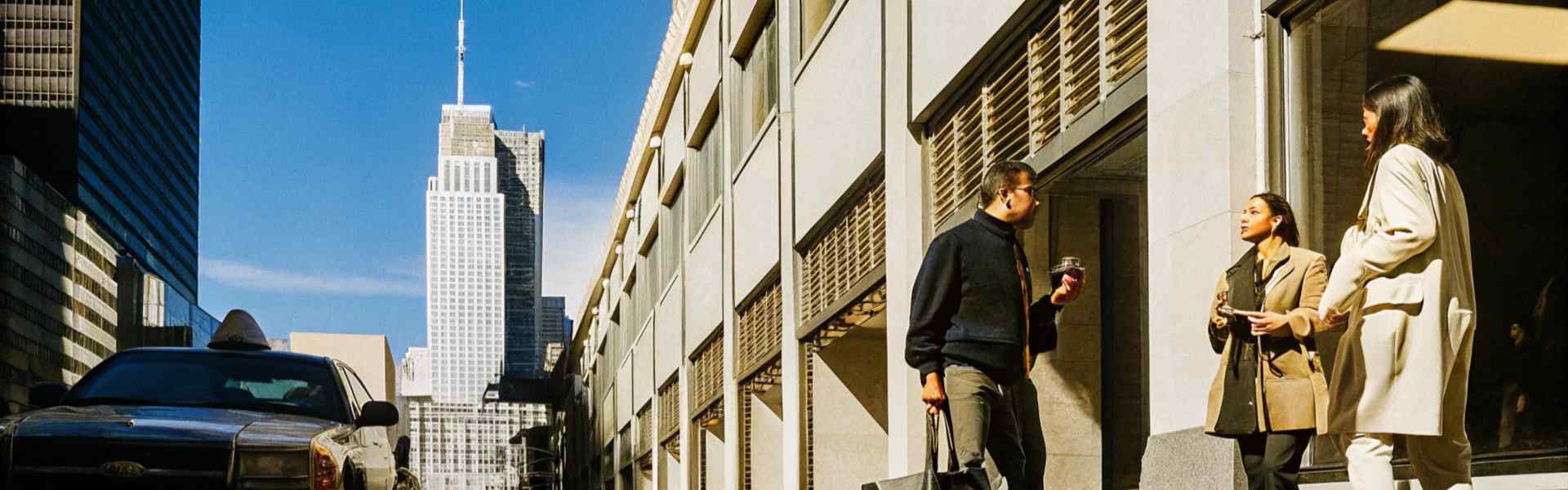 People talking outside a modern building under a clear blue sky with a tall skyscraper in the background.