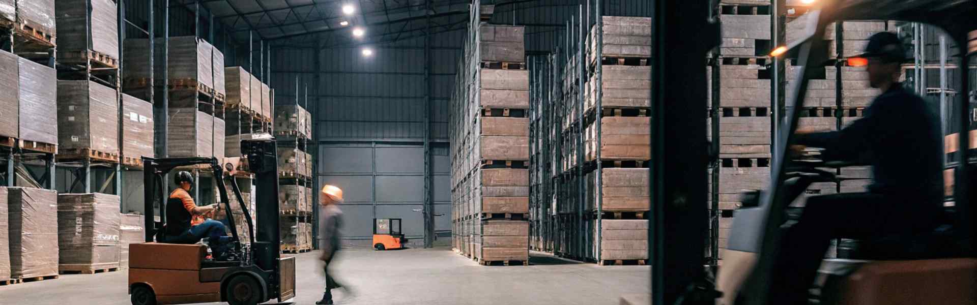 Forklifts operating in a large warehouse with high shelves and stacked pallets.