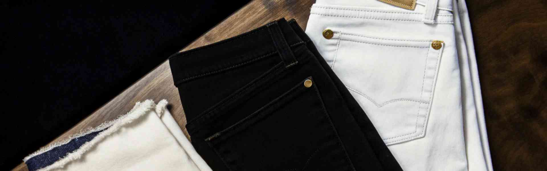 Flat lay of black and white jeans on a wooden surface.