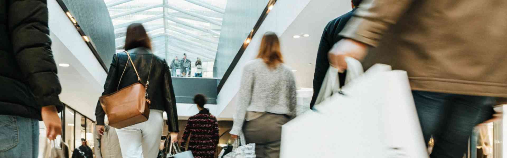 Shoppers walking through a mall carrying multiple shopping bags.