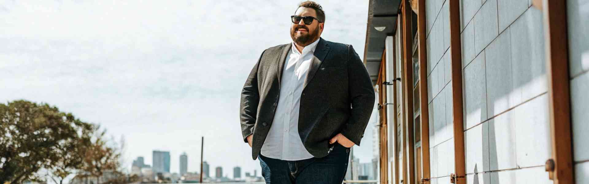 A stylish man in a blazer, white shirt, and jeans walking outdoors.