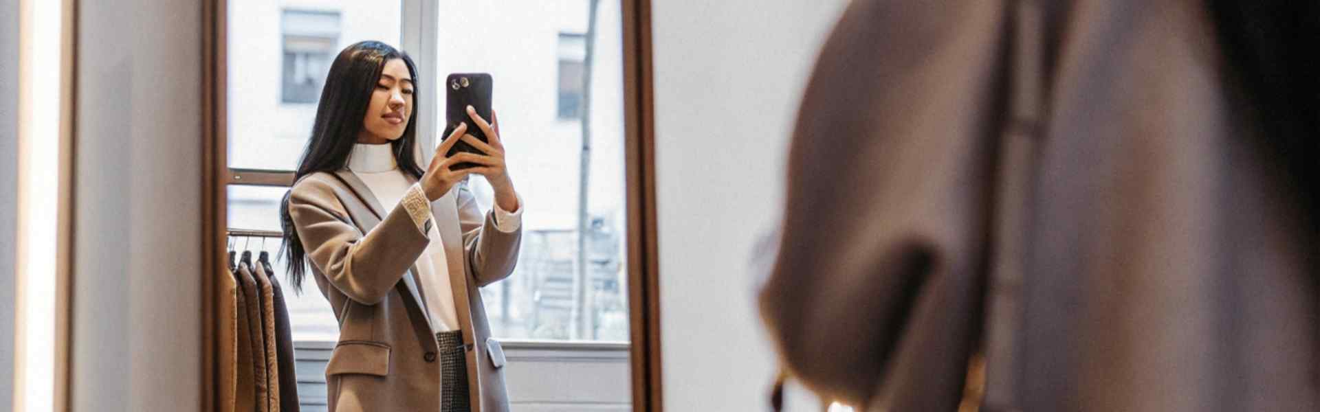 Woman taking a mirror selfie in a stylish outfit inside a clothing store.